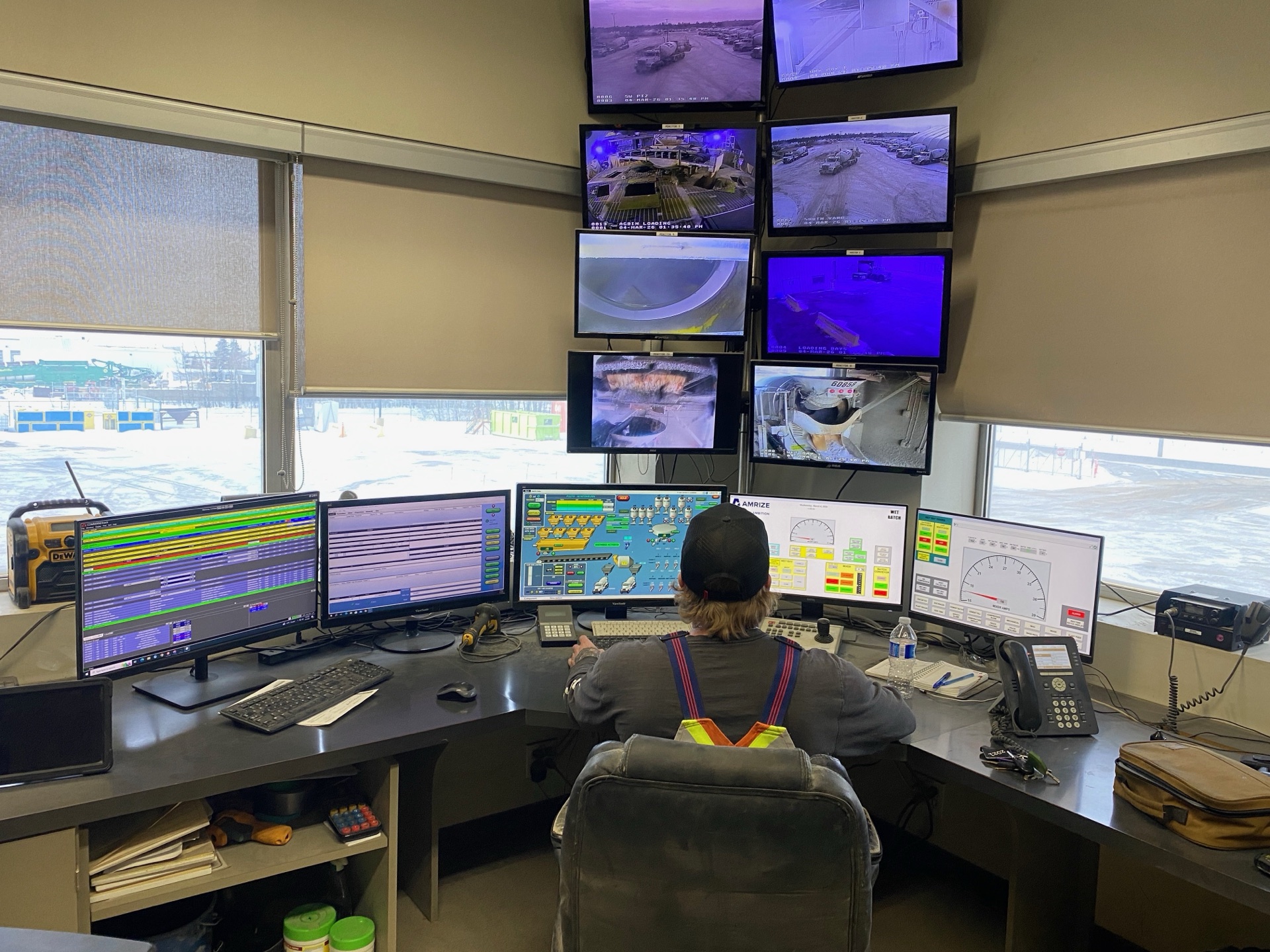 Operator monitoring a concrete batch plant from a control room with CCTV feeds