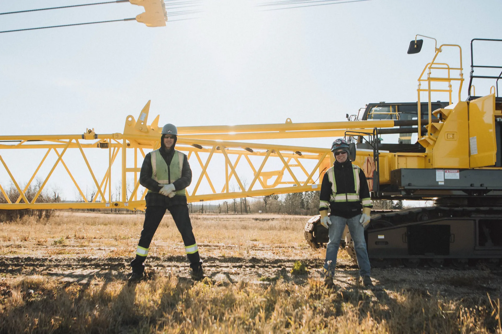 Two operating engineers in front of a yellow crawler crane with lowered lattice boom
