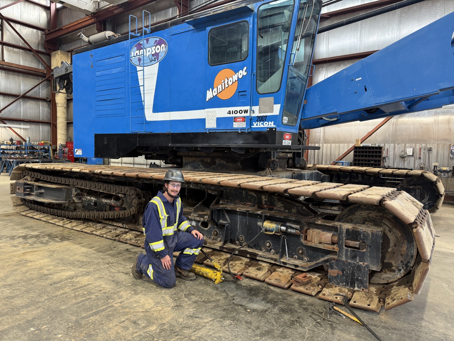 Mechanic beside the crawler track of a Lampson Manitowoc 4100W crane in a shop