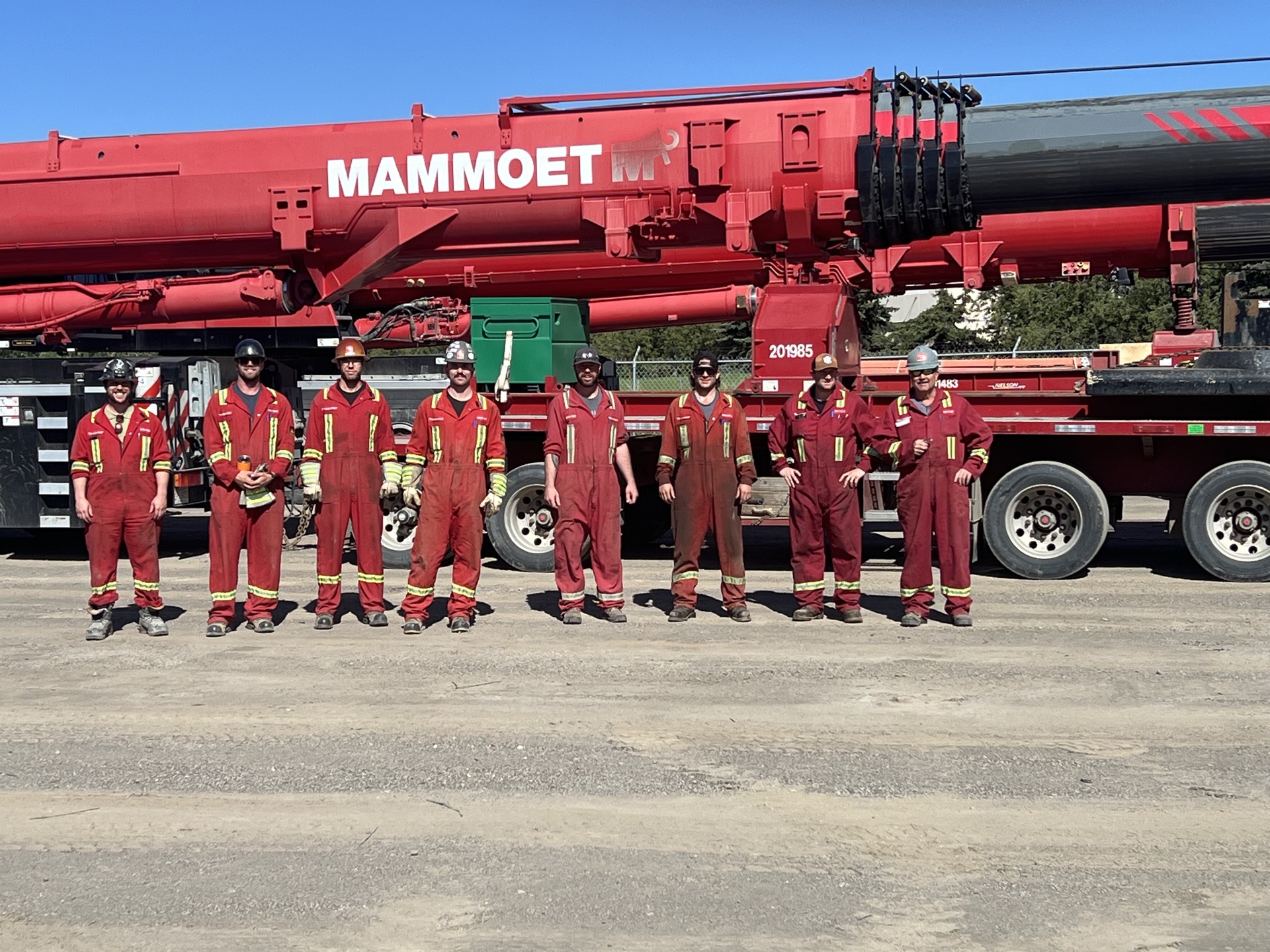 Crew of eight operating engineers posing in front of a red Mammoet mobile crane