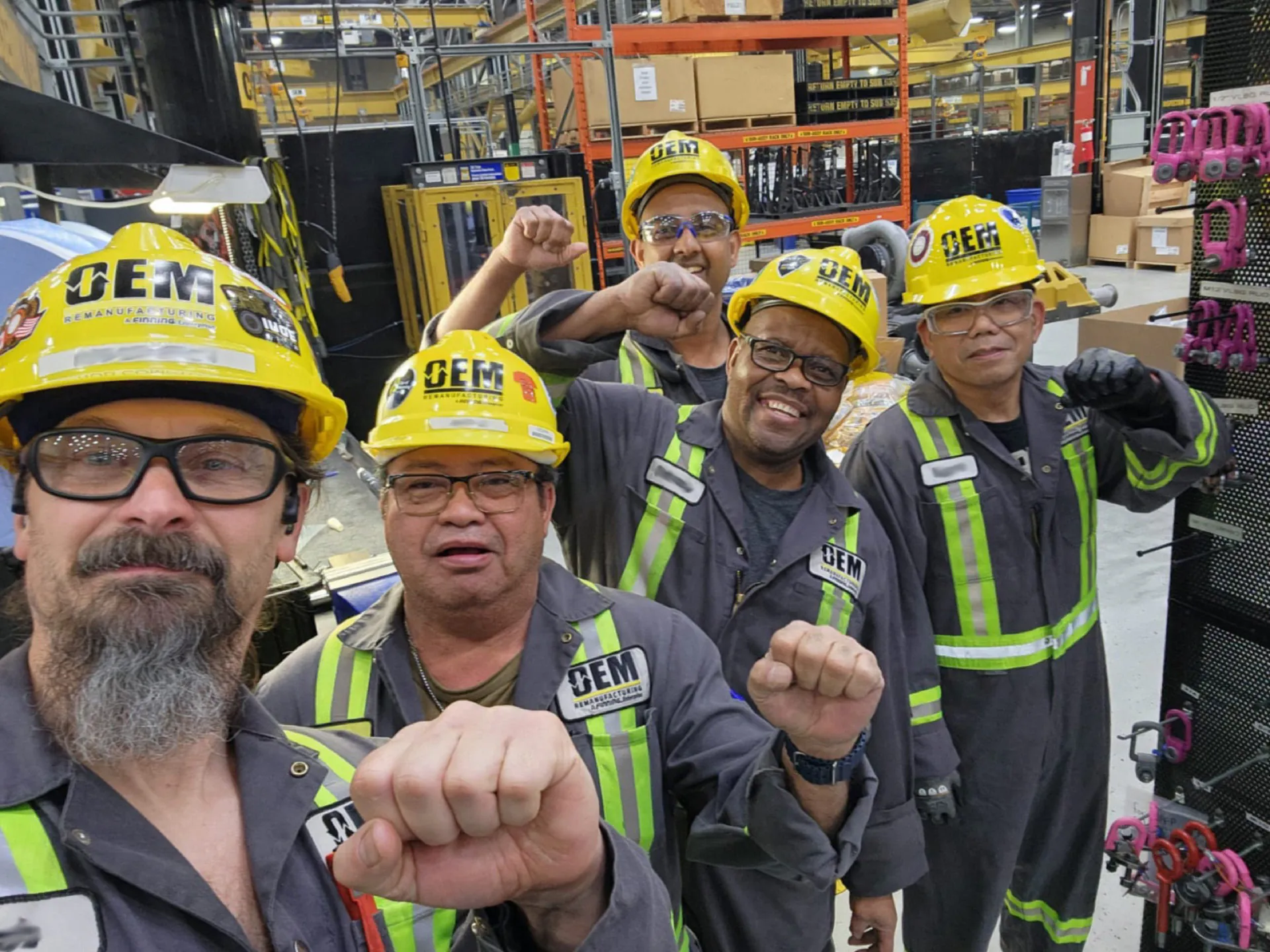 IUOE Local 955 members in OEM Remanufacturing hard hats raising fists in solidarity in a parts warehouse