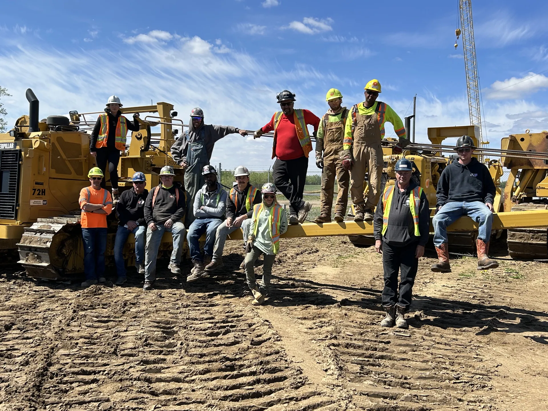 Pipeline crew posing on a Caterpillar sideboom pipelayer at a muddy jobsite